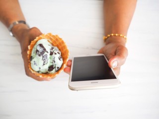 Woman eating mint ice cream with smart phone