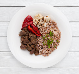 Buckwheat porridge, beef meat and grilled vegetables top view. Healthy food, sport diet, lunch dish concept. White wooden planks background.