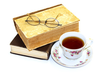 On an old book with a torn binding. broken spine are glasses and a cup of tea