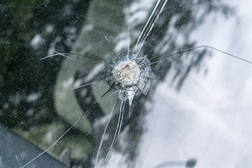 Broken car windshield with radial cracks and a hole in the middle.