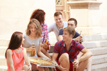 Young friends sitting on stairs with pizza and beer