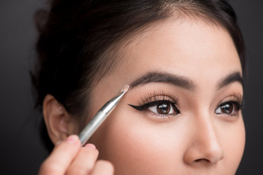 Close Up Of Beautiful Face Of Young Asian Woman Getting Make-up. The Artist Is Applying Eyeshadow On Her Eyebrow With Brush