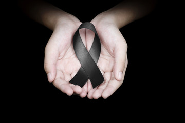 Hand holding black ribbon on black background mourning awareness sign