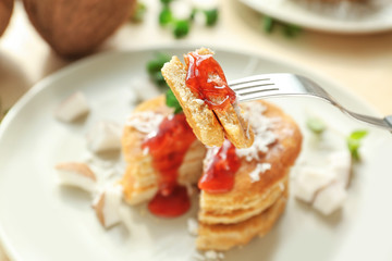 Pieces of tasty coconut pancakes with berry sauce on fork, closeup