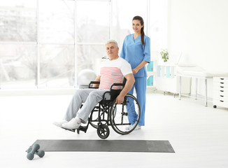 Senior disabled man with young orthopedist in rehabilitation clinic