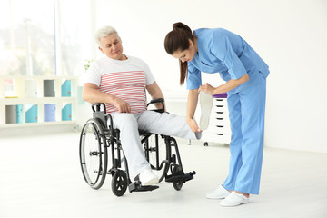 Senior disabled man with young orthopedist in rehabilitation clinic