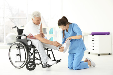 Senior disabled man with young orthopedist in rehabilitation clinic