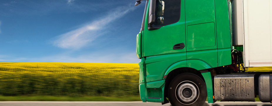 gr&uuml;ner LKW f&auml;hrt vor einem Rapsfeld mit blauem Himmel Panorama