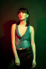 Stylish woman in leather pants in red and green light. Studio photo. Beauty and fashion