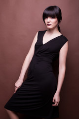 Woman in long black dress on brown background in studio photo. Beauty and fashion. Model test