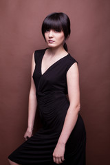 Fototapeta premium Woman in long black dress on brown background in studio photo. Beauty and fashion. Model test