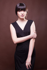 Obraz premium Sensual woman in long black dress on brown background in studio photo. Beauty and fashion. Model test