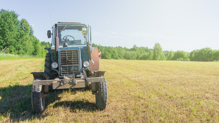 Naklejka premium red old rusty tractor in a field of mown grass against a forest background in good weather