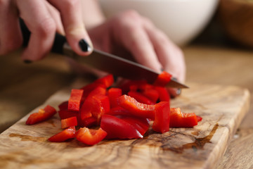 young female hands chopping red bell pepper on kitchen table