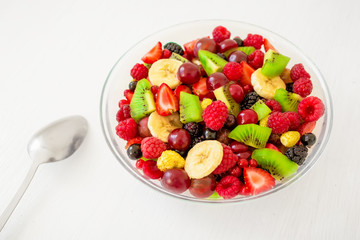 Bowl of healthy fresh fruit salad on white wooden background. Top view.