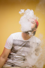 Men spray cigarette smoke under the light on yellow background