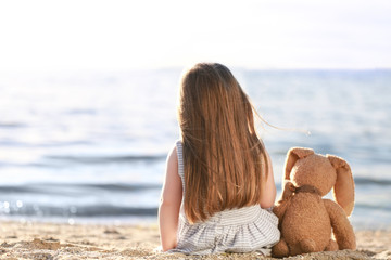 Cute little girl with bunny toy sitting near river