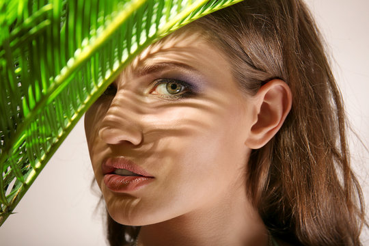 Portrait of beautiful young woman with palm leaves on light background, closeup