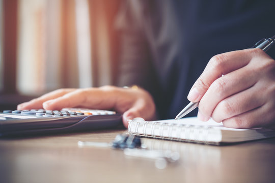 Closeup image of a business woman working , writing on notebook and using calculator in office