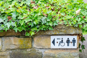 Schild WC für Behindere, Frauen und Männer an einer Mauer