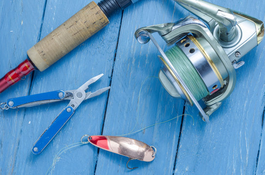 Spinning, reel, yellow-red fishing spoon and pliers. The bait and the tool of a fisherman.