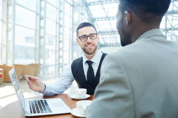 Portrait of smiling businessman talking with African-American man, discussing work during meeting in modern office building