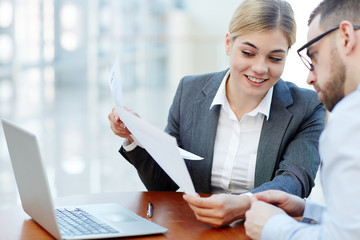 Portrait of smiling young businesswoman showing documents to her colleague during meeting