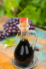 Black old balsamic vinegar in a glass jug with fresh red grapes on green vineyard background