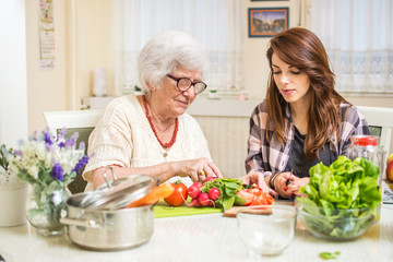 Grandmother and granddaughter preparing food together at kitchen.