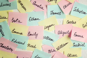 Closeup of paper stickers with different names on white wall. Concept of choosing baby name - obrazy, fototapety, plakaty