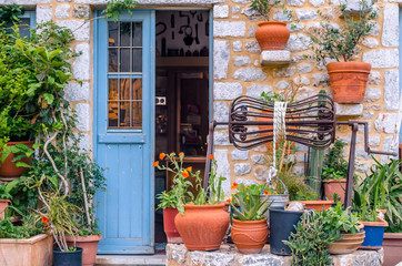 Fototapeta na wymiar A yard in a traditional stone house with pots full of flowers and a well in front of a light blue wooden door.