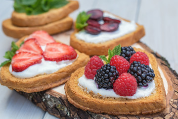 Heart shaped biscuits spread with quark, strawberries, blackberries, raspberries, cherries and a twig of mint presented on a tree disk