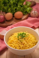 Instant noodles in bowl with vegetables on wood background