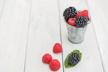 Small metal bucket filled with raspberries, blackberries and a sprig of mint.
