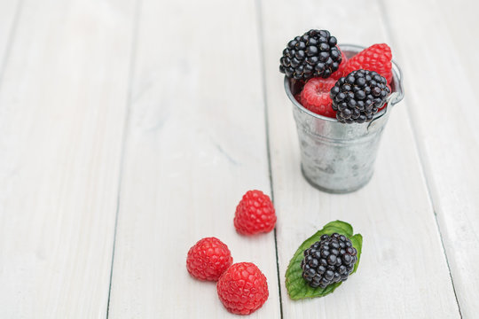 Small metal bucket filled with raspberries, blackberries and a sprig of mint.