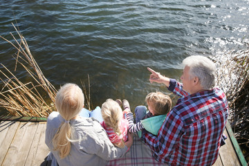 Happy grandparents with little children near river on sunny day