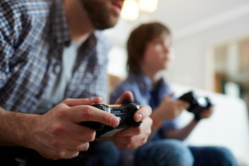 Young man with joystick playing video game on background of his son © pressmaster