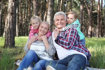 Happy grandparents with little children sitting on grass in forest