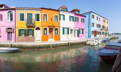 Burano, Venice, Veneto, Italy, Row of colorful fisherman houses on a canal with reflections in a panorama view. Burano island is famous for its lace and brightly colored buildings 