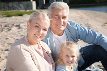 Happy grandparents with little girl sitting on river bank