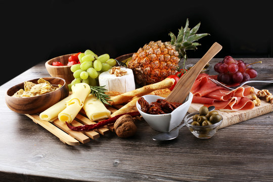 Italian antipasti wine snacks set. Cheese variety, Mediterranean olives, pickles, Prosciutto di Parma over black grunge background