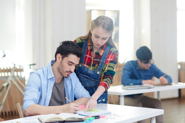 Two friendly students discussing task in notebook