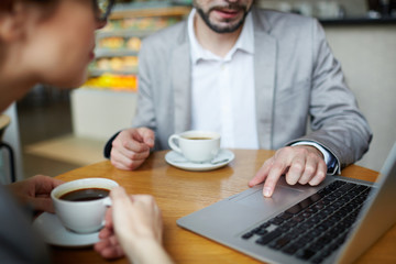 Portrait of two business people meeting in cafe and using laptop at table, finger on touchpad closeup