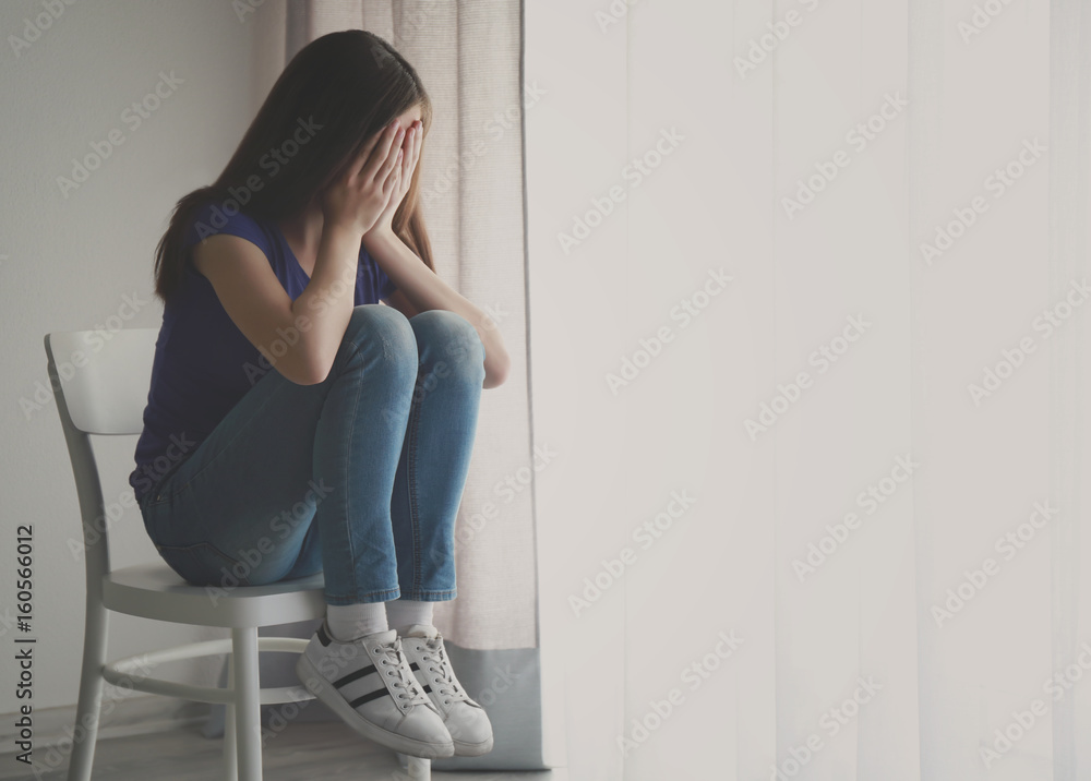 Wall mural Cute sad girl near window at home