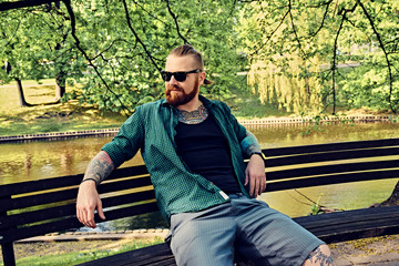 Bearded male sits on a bench in a park.