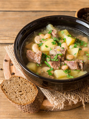 Beef soup with potatoes, beans and leeks in ceramic bowl on stone background.