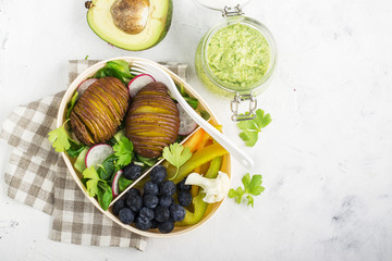 Healthy snack in a lunch box: Golden baked potatoes, salad, blueberries, green pepper, cauliflower, radish in a plastic container with a fork. Top view