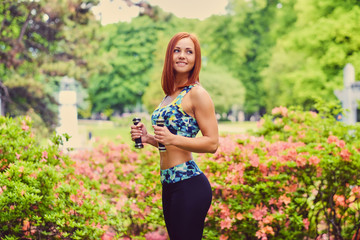 Portrait of redhead fitness female holds dumbbells.