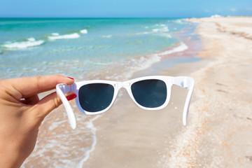 Fototapeta na wymiar Sunglasses in hand on background of the beach