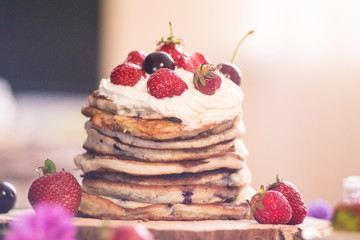 Delicious pancakes with berries and cream on the authentic wooden stand. Summer food still life concept.